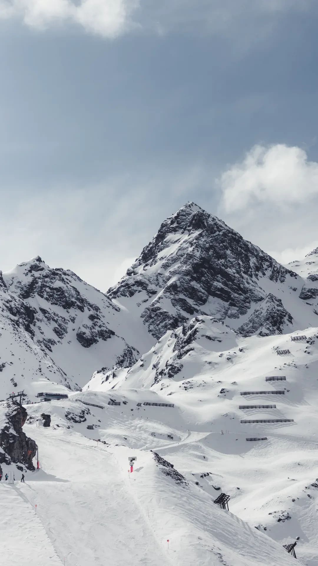 Verschneiter Gipfel mit Lawinenverbauungen, Wolken ziehen vorbei