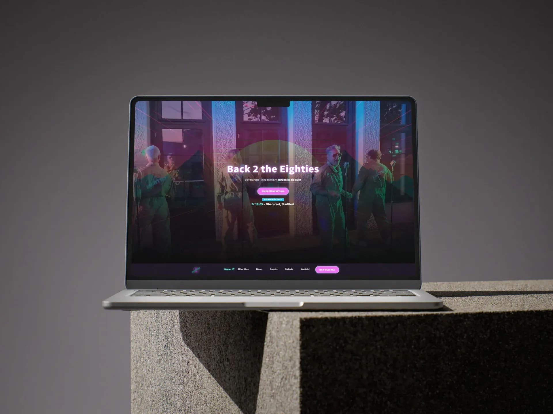 Die Startseite von Back 2 the Eighties auf einem Laptop: Bandfoto in Neonfarben, darüber der Schriftzug und der nächste Auftritt