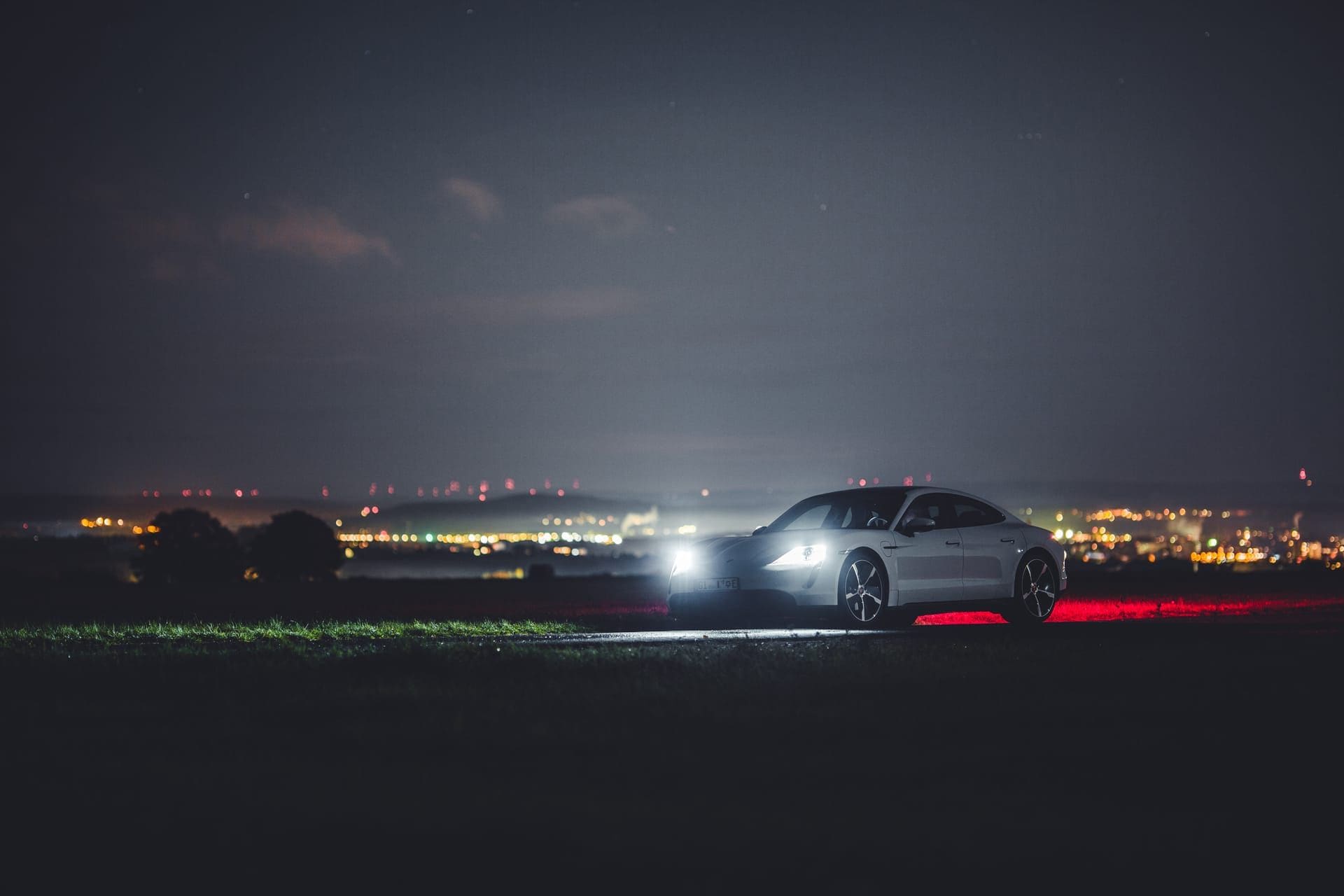 Sportwagen bei Nacht vor den Lichtern einer Stadt im Tal