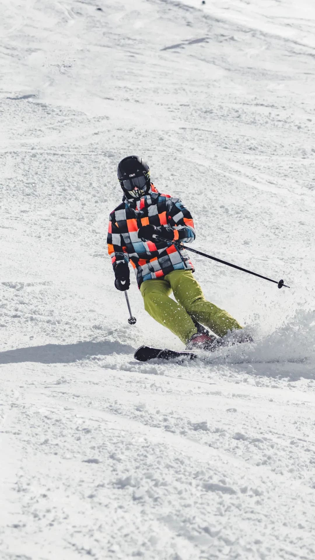 Skifahrer in bunt karierter Jacke schwingt auf der Piste ab