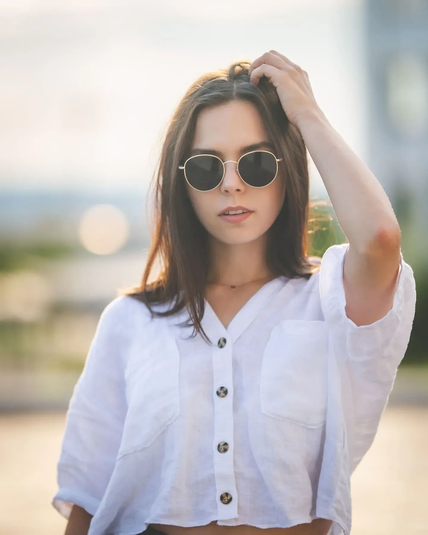 Junge Frau mit runder Sonnenbrille und weißer Leinenbluse, Hand im Haar