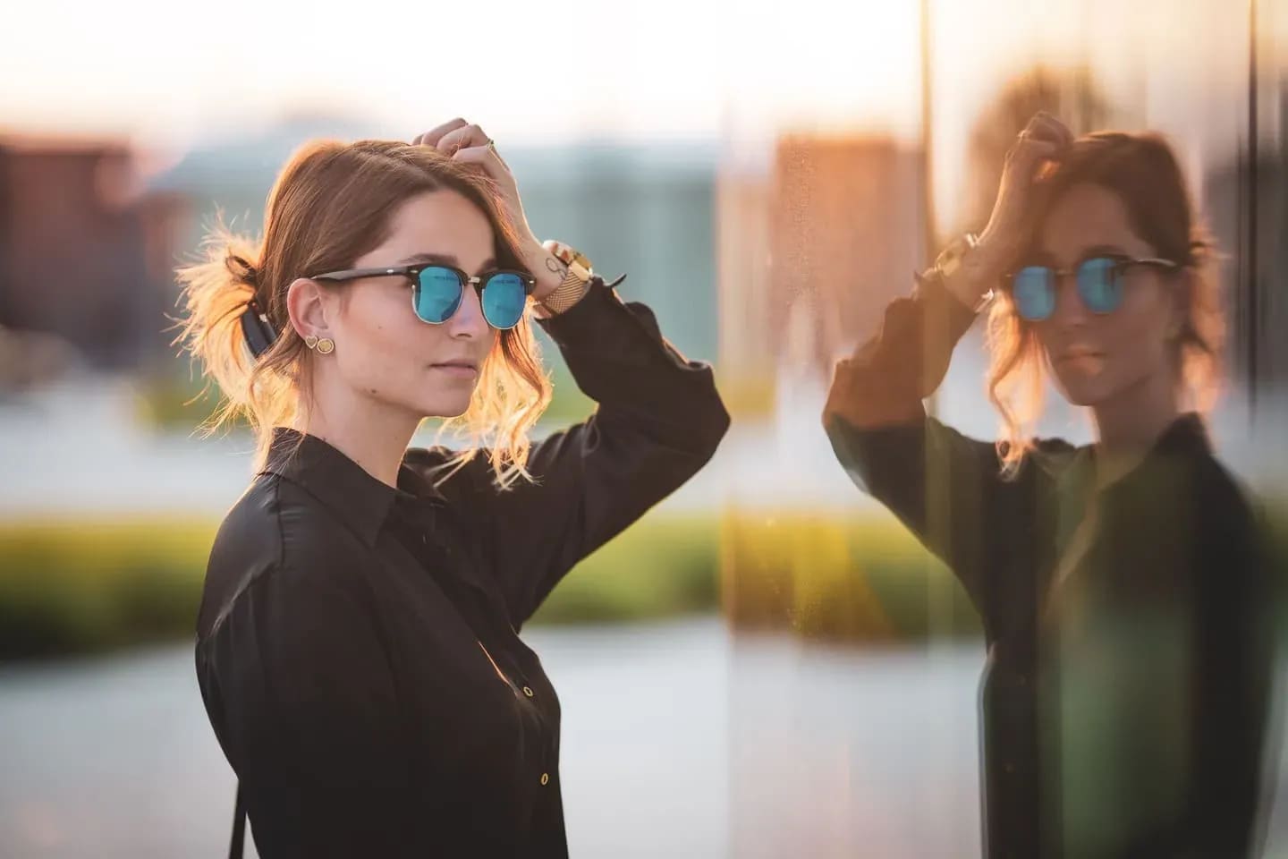 Junge Frau vor einer Glasfassade, ihre Spiegelung daneben, Abendsonne