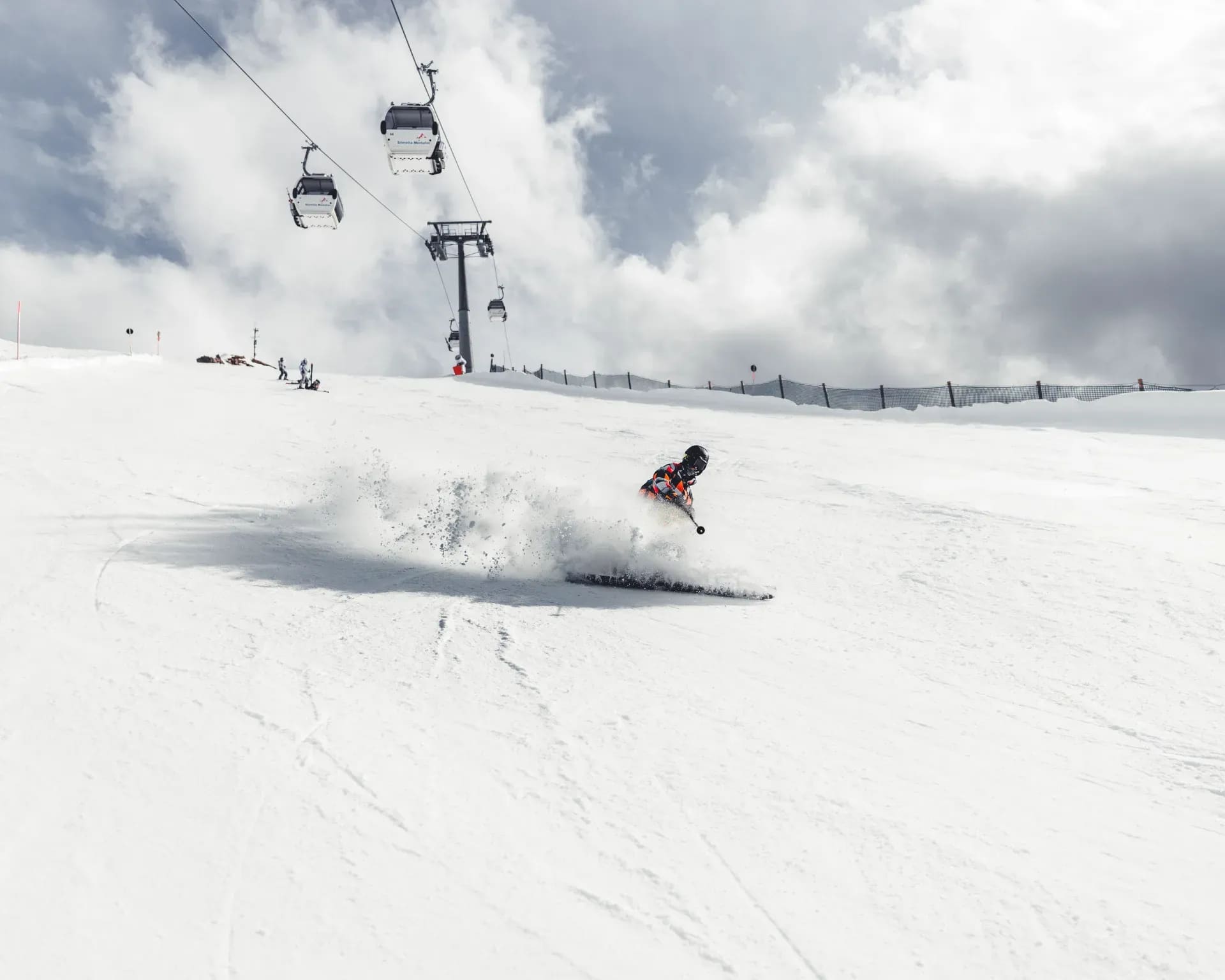Skifahrer in der Abfahrt, darüber die Kabinen der Gondelbahn