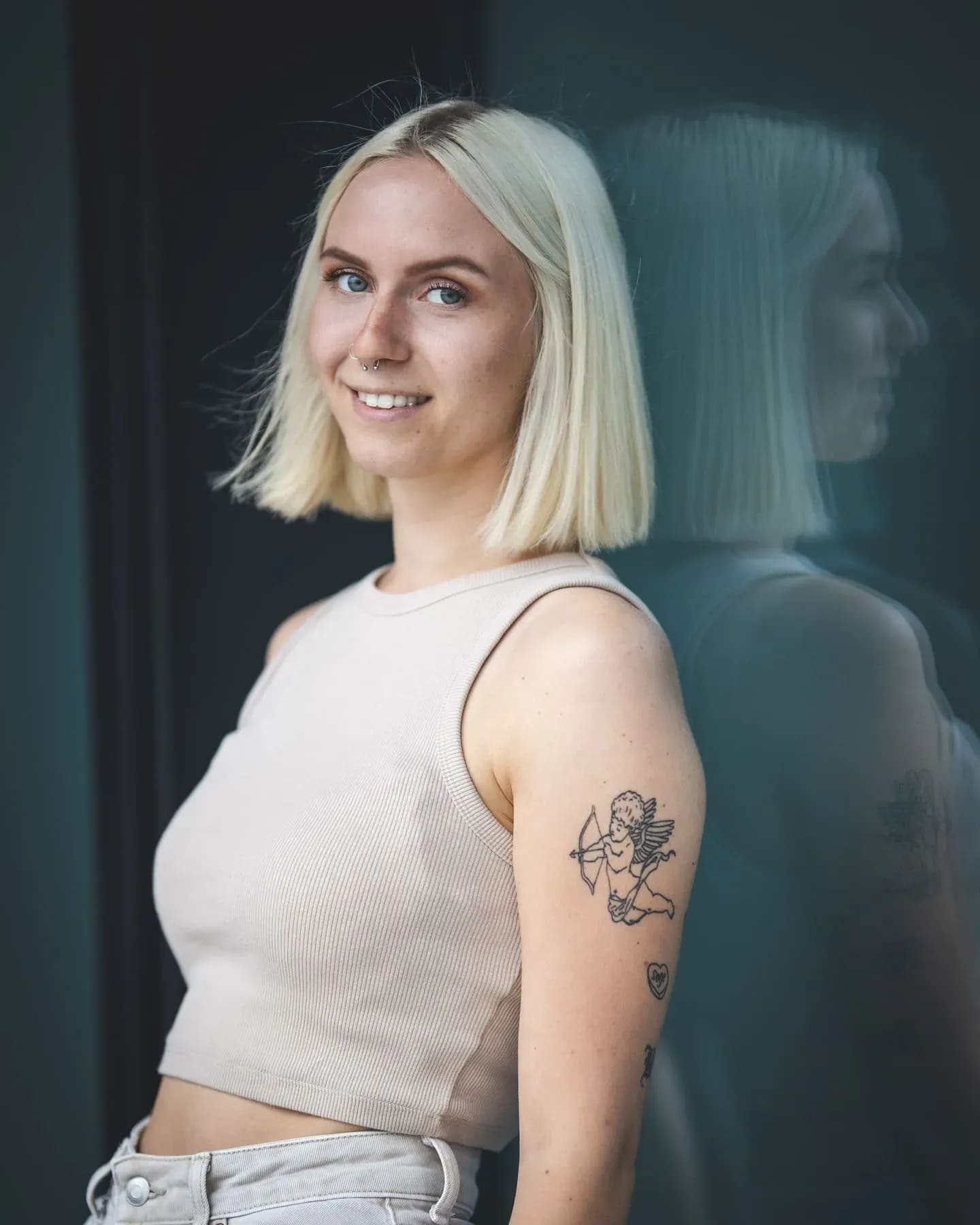 Junge Frau im beigen Top mit Tattoo am Arm, Spiegelung in einer dunklen Scheibe