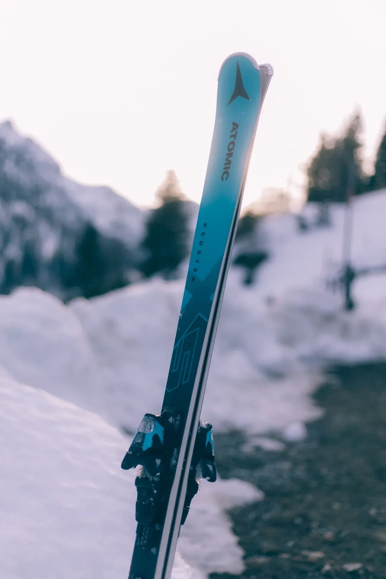 Ein Paar Ski steckt aufrecht im Schnee, Berge dahinter