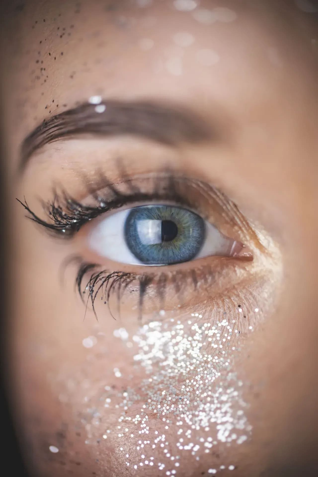 Makroaufnahme eines blauen Auges, Glitzer auf Braue und Wange