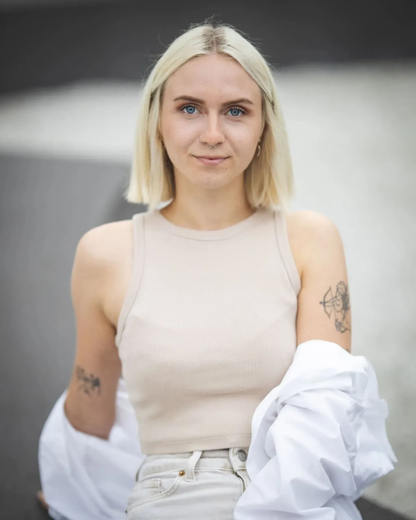 Junge Frau im beigen Top mit Tattoos, weißes Hemd über den Armen