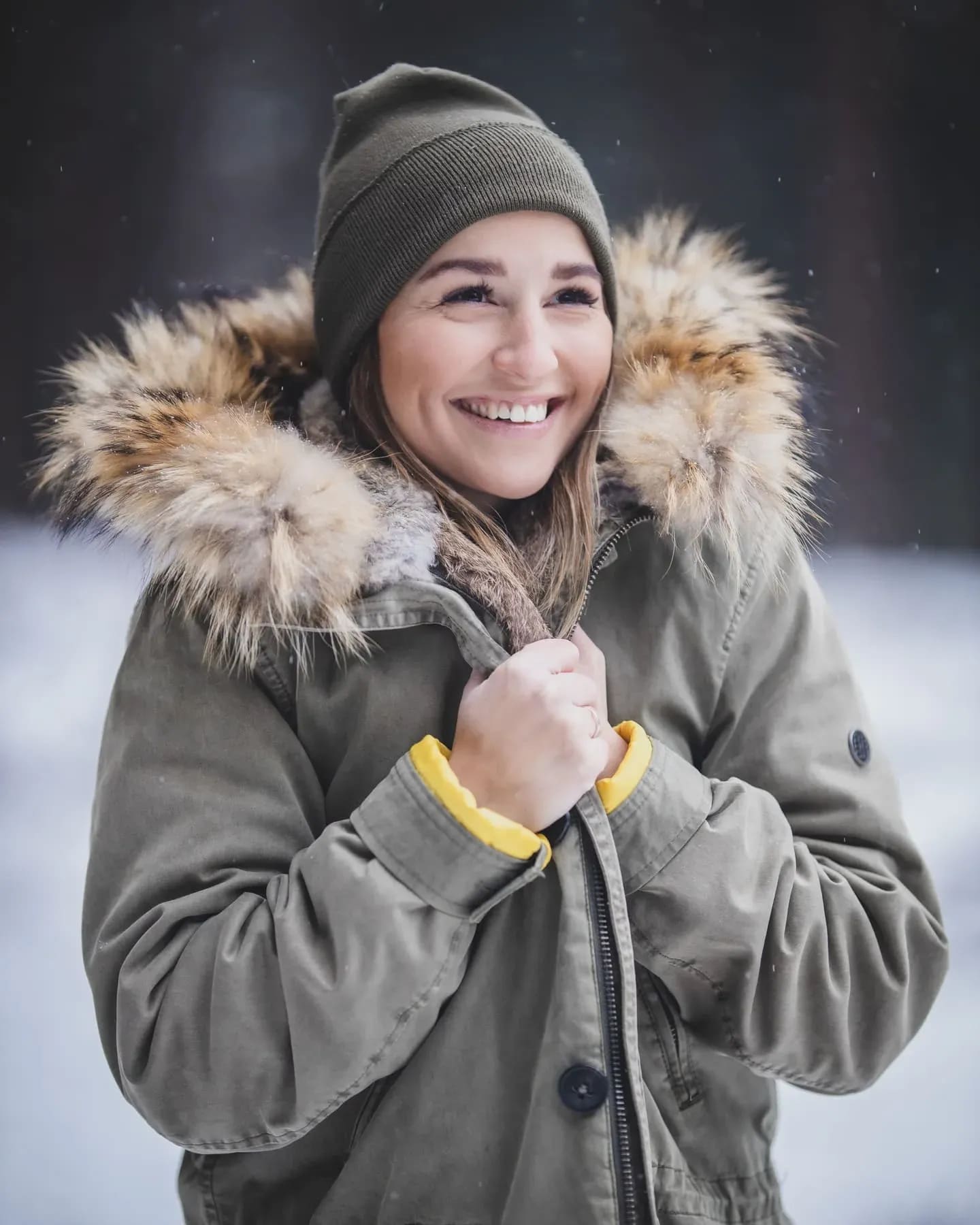 Lachende Frau in Winterjacke mit Fellkapuze und Mütze