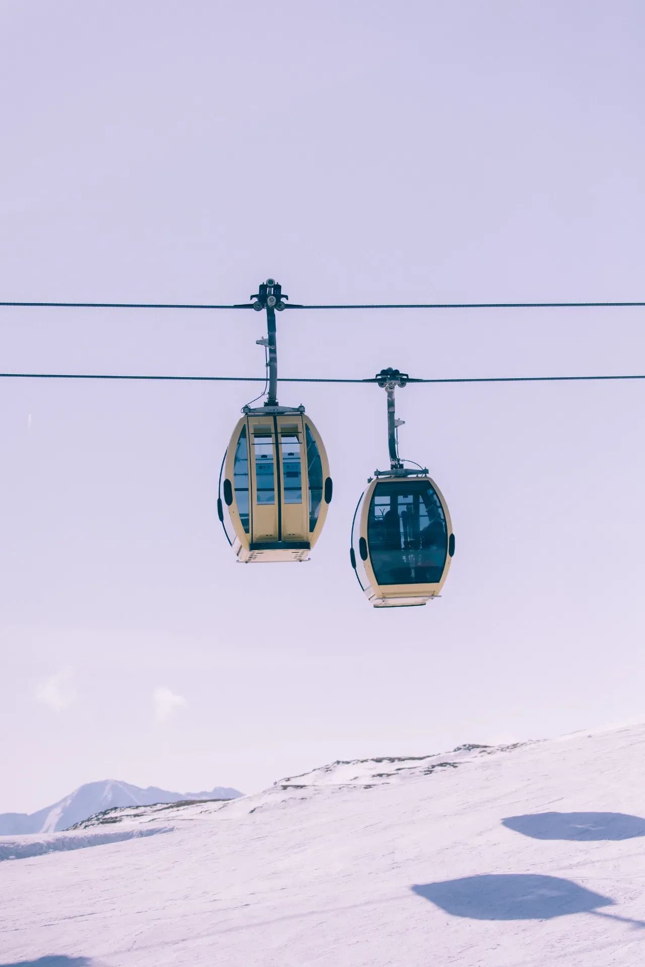 Zwei gelbe Gondeln vor blauem Himmel über dem Hang