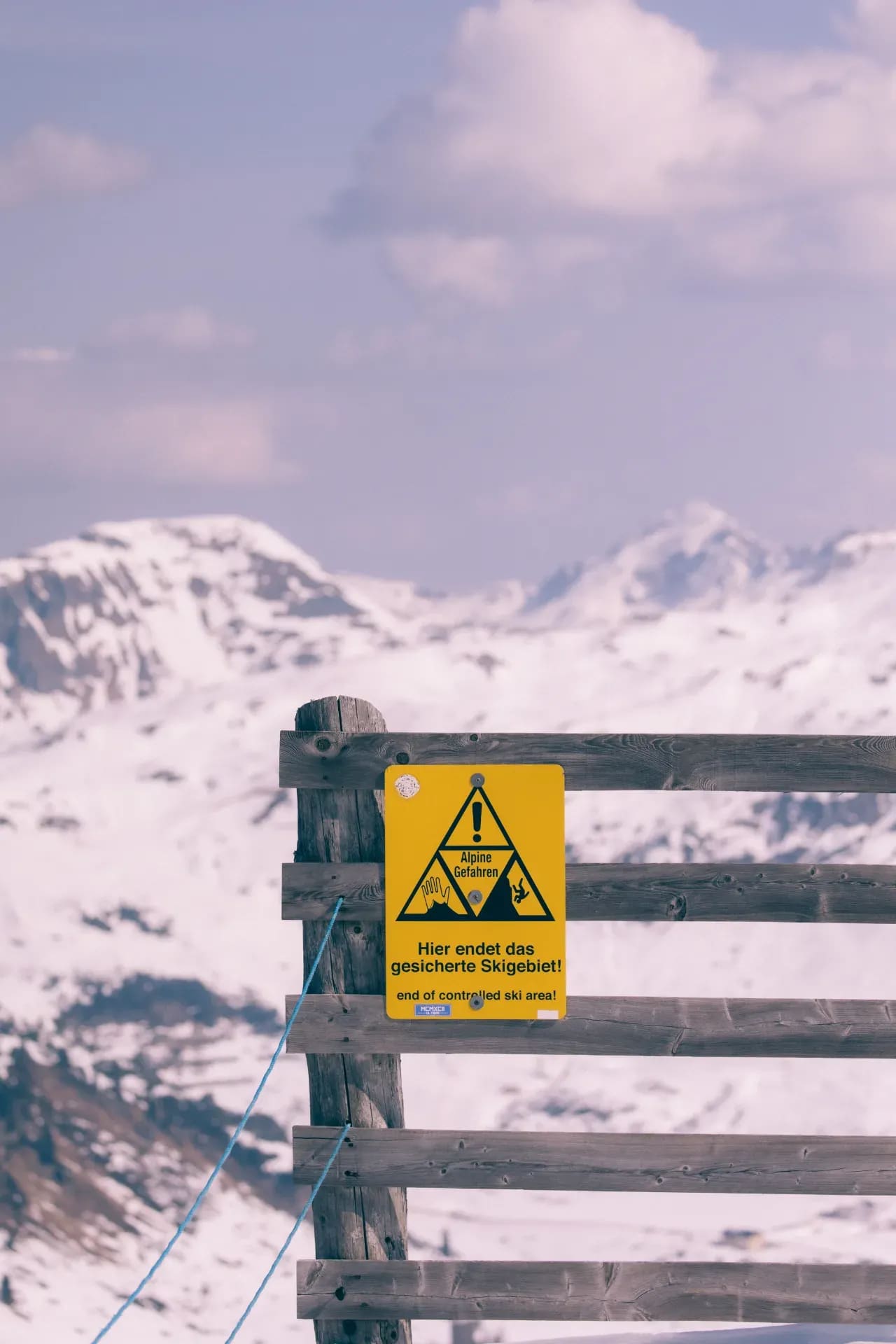 Warnschild am Ende des gesicherten Skigebiets, Berge dahinter