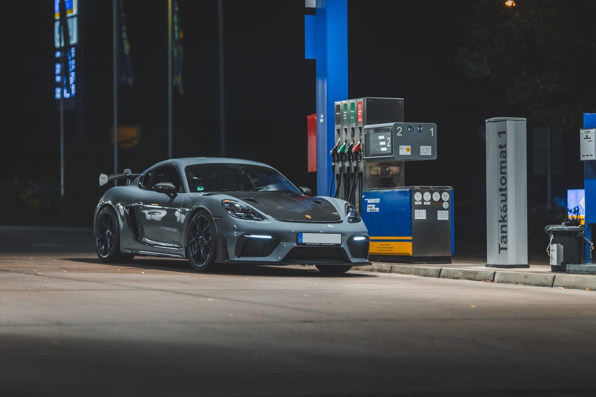 Grauer Sportwagen nachts an einer beleuchteten Tankstelle