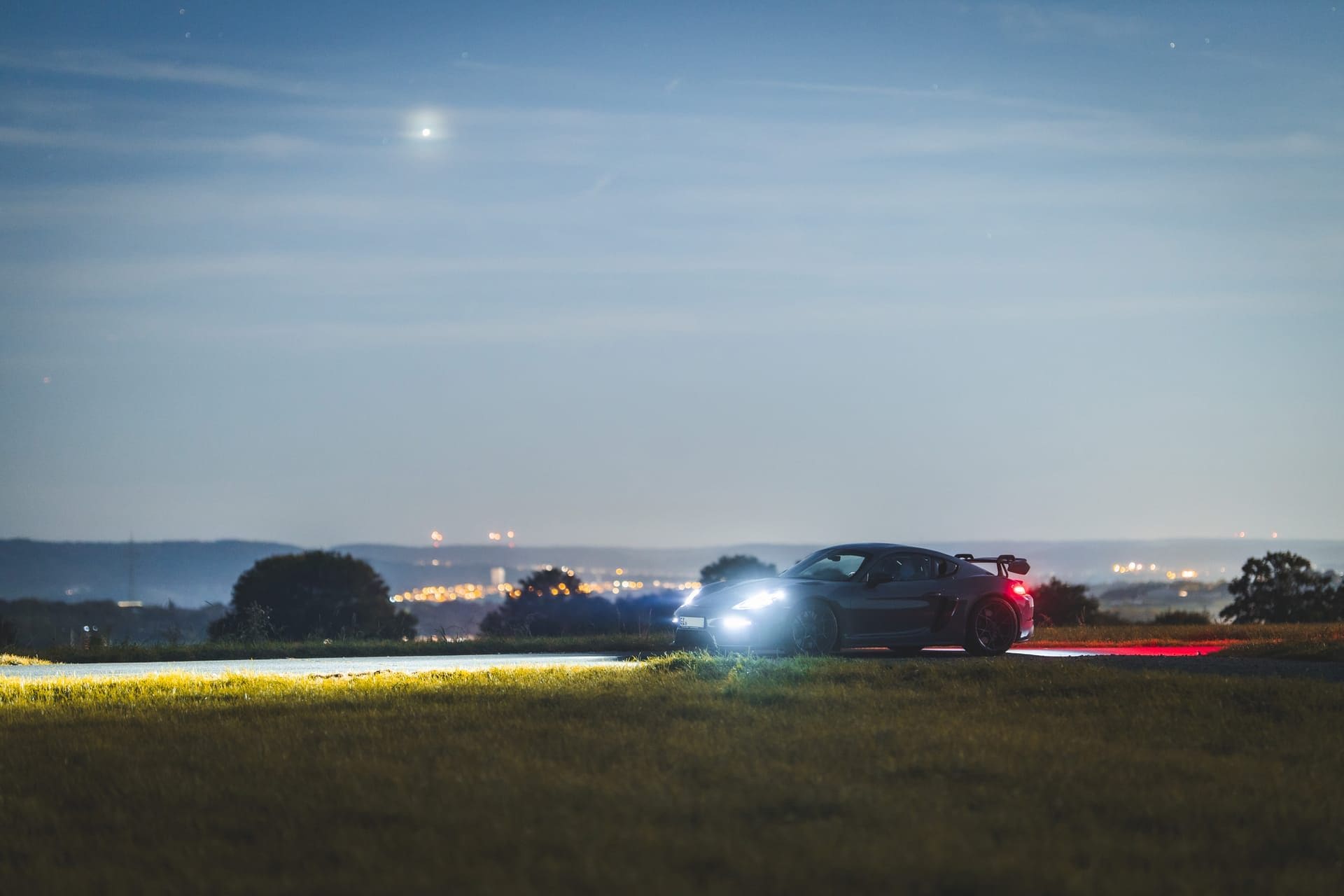 Sportwagen in der Dämmerung auf einer Anhöhe, im Tal die Lichter der Stadt