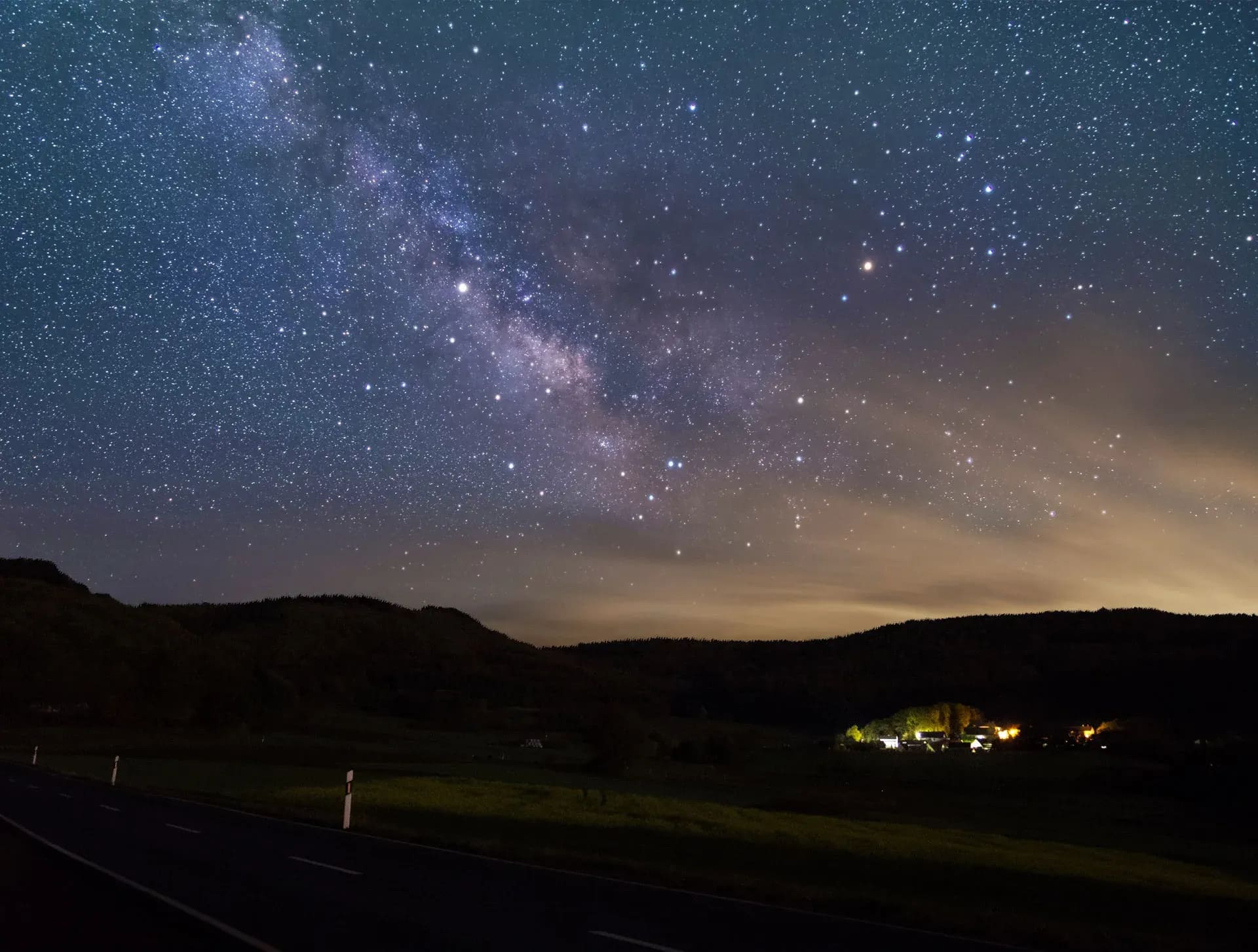Milchstraße über einer Landstraße, Ortschaft im Tal