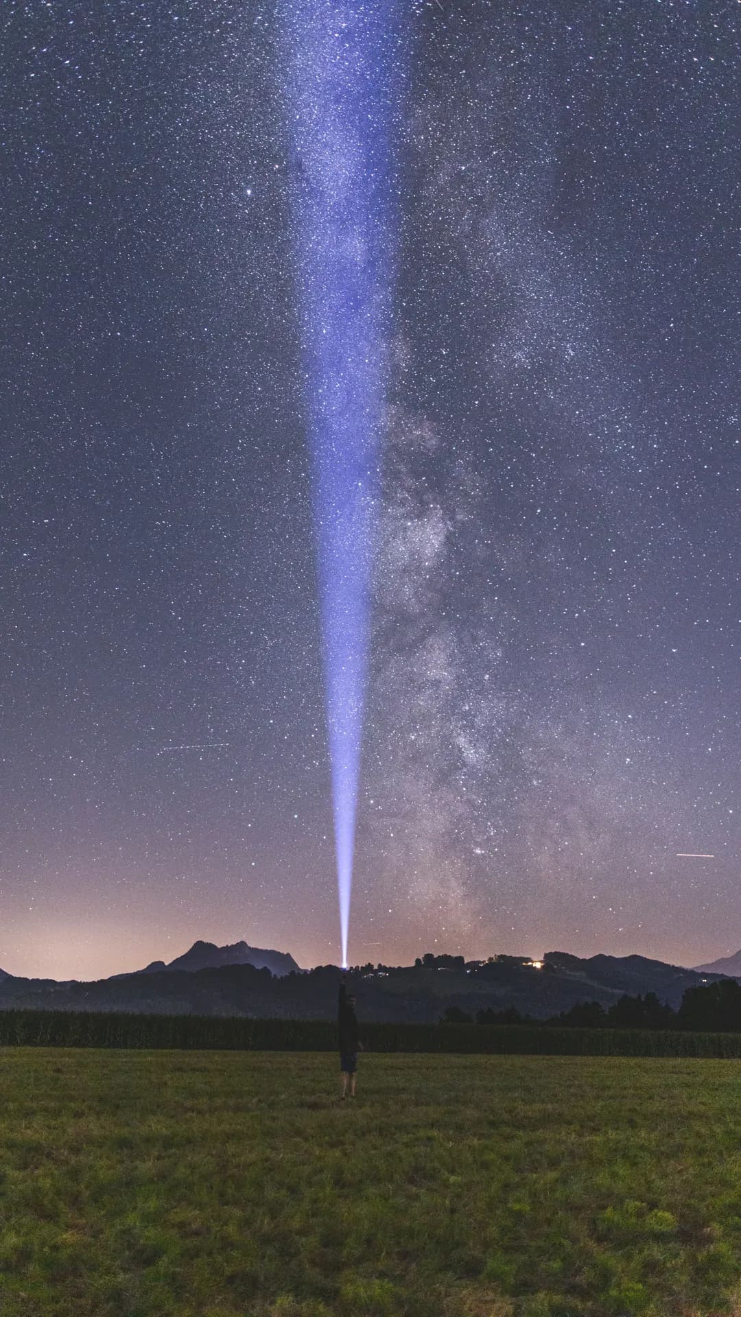 Lichtstrahl zeigt in die Milchstraße über einer Wiese