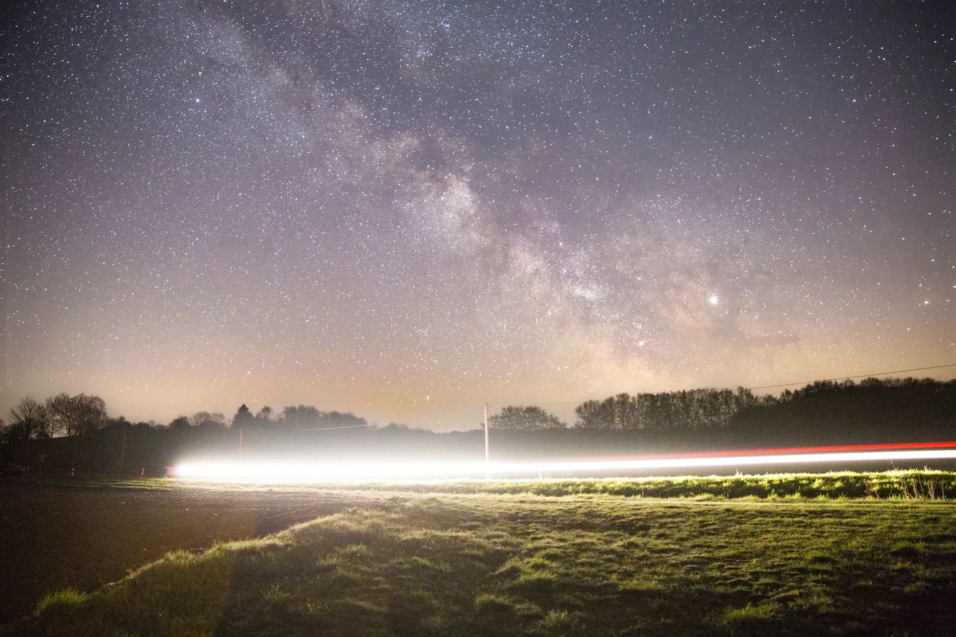 Milchstraße über einer Wiese, Lichtspur eines Autos