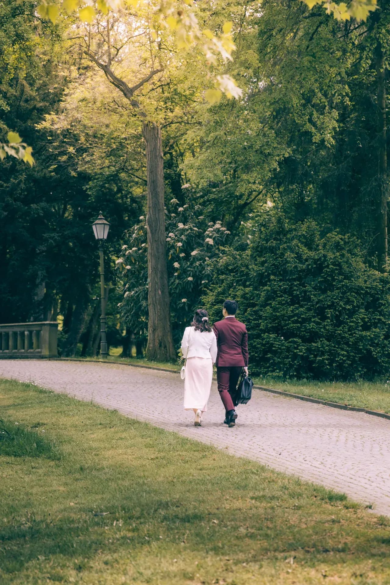 Paar geht einen Parkweg entlang, hohe Bäume zu beiden Seiten