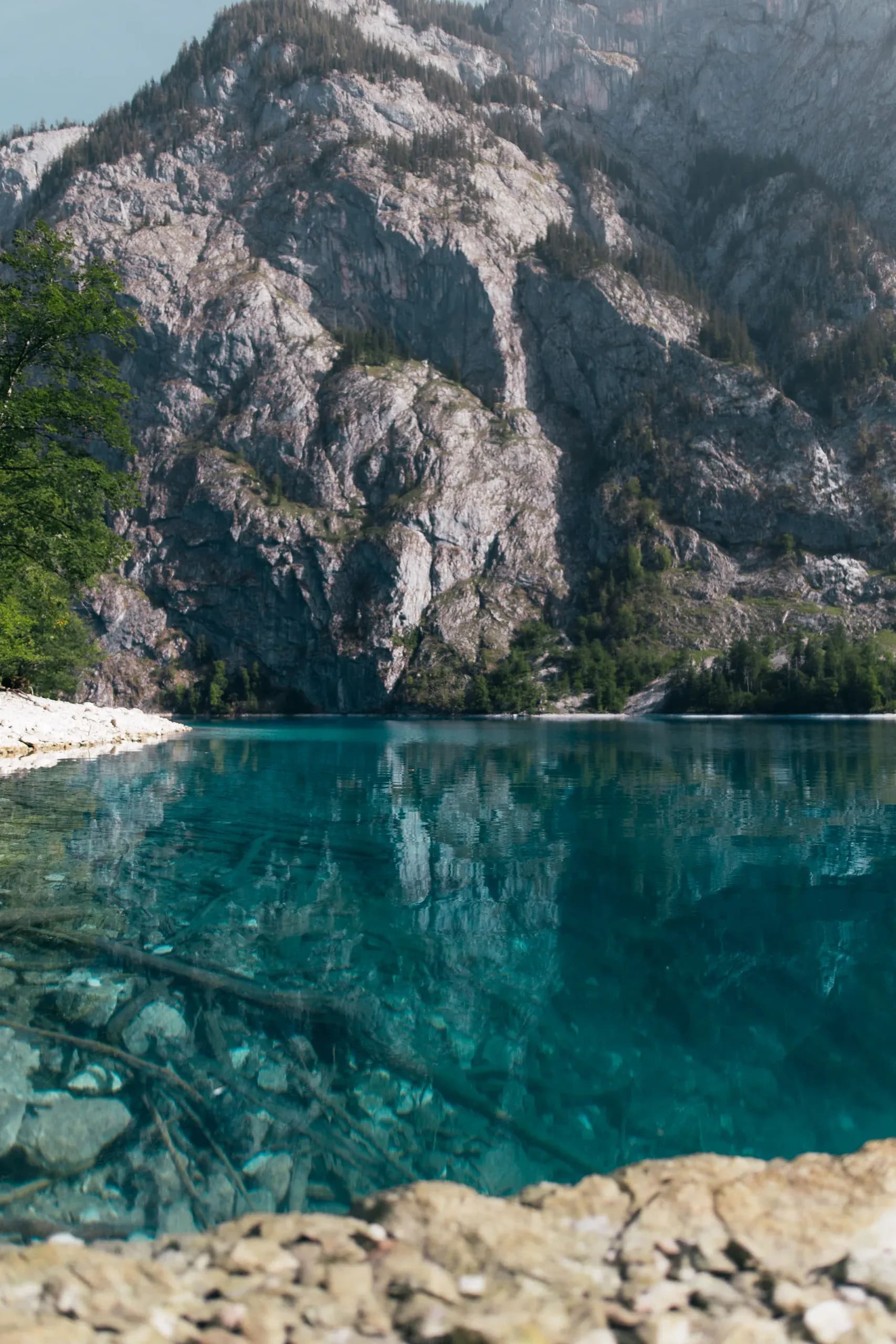Steiniges Ufer am türkisen Wasser, Felswand darüber