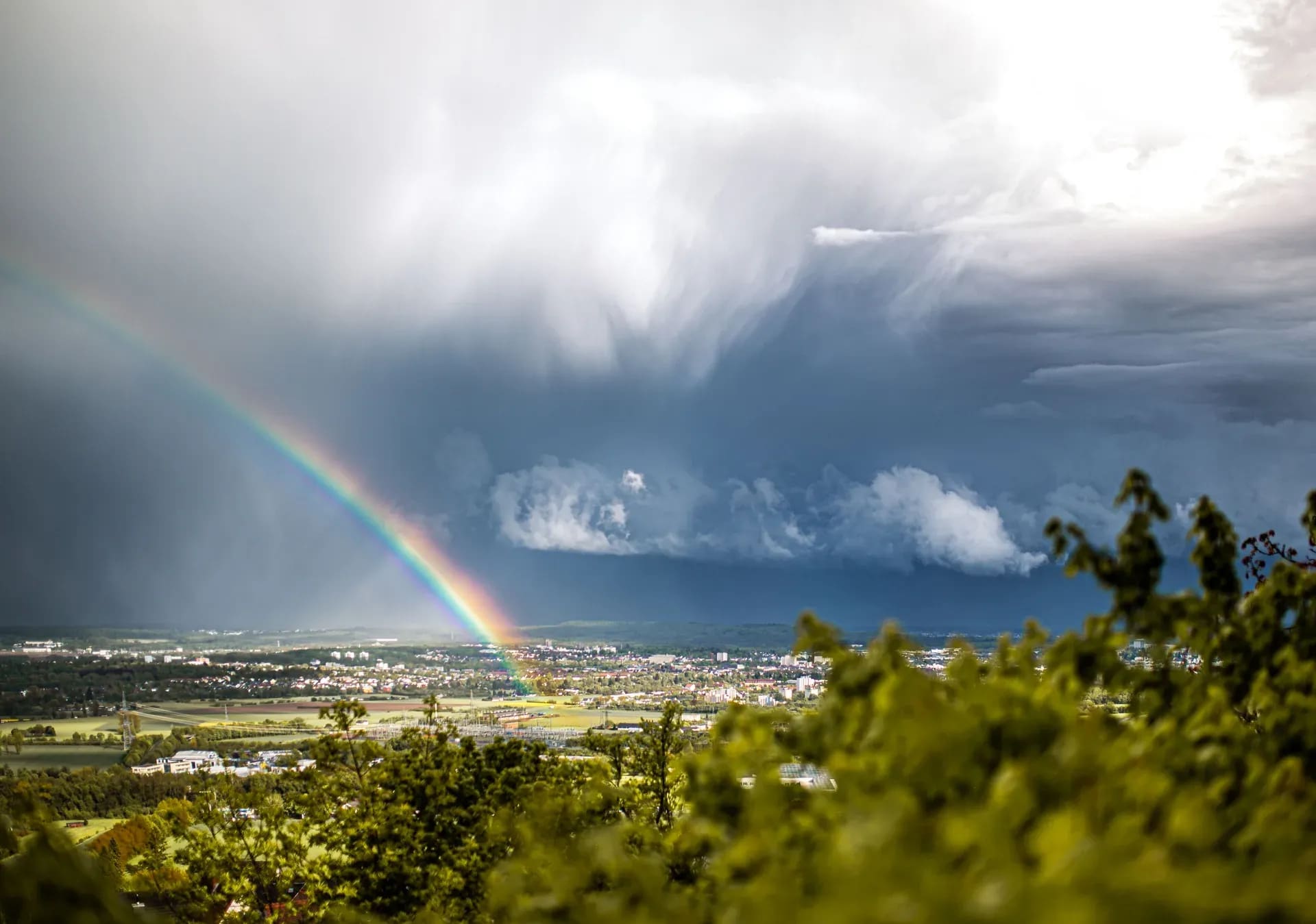 Regenbogen vor einer Gewitterwolke über der Stadt