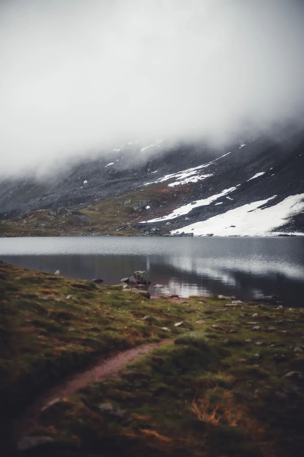Bergsee mit Schneeresten im Nebel
