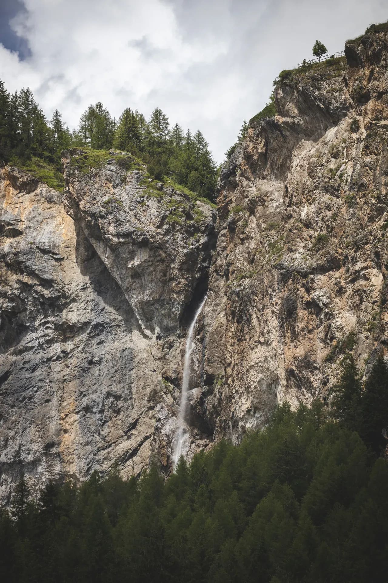 Wasserfall in einer Felswand über Nadelwald